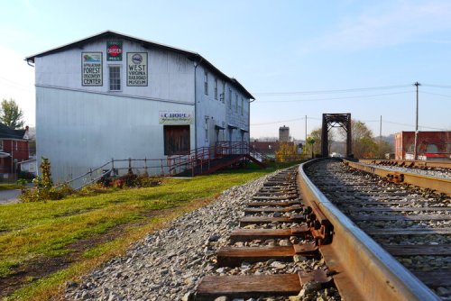 A railway track curves beside a gray building with signs, set against a clear sky and distant townscape.