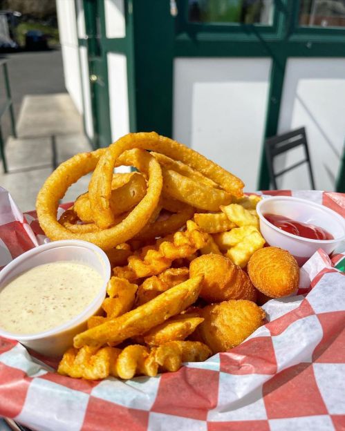 A basket of crispy fried snacks including onion rings, crinkle fries, and dipping sauces.