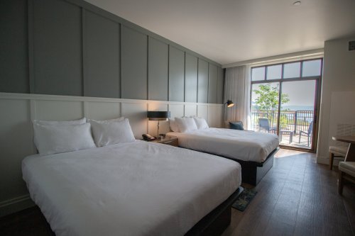 A hotel room featuring two beds, a balcony with a view, and modern decor in neutral tones.