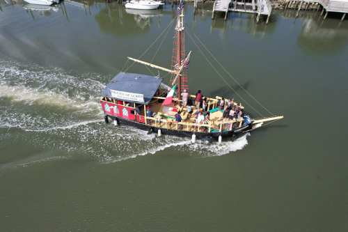 A colorful boat with passengers sails through calm waters, leaving a wake behind as it navigates the harbor.