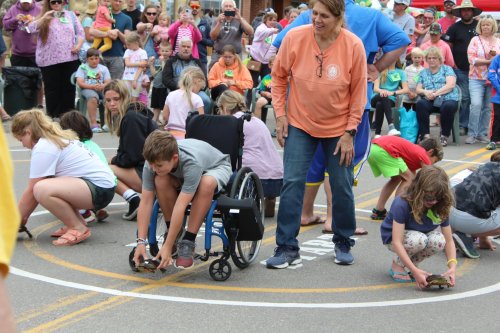 A group of children and adults participate in a turtle race, with spectators watching in the background.