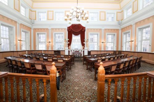 Interior of a historic courtroom with wooden furniture, large windows, and decorative chandeliers.