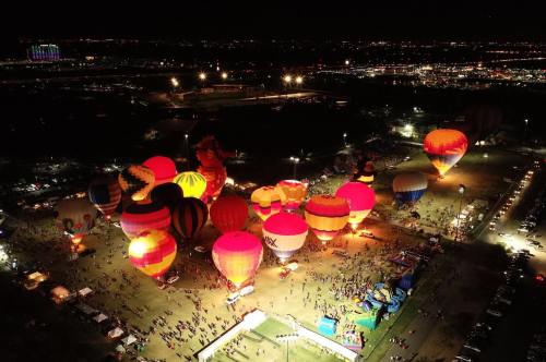 Aerial view of colorful hot air balloons illuminated at night, surrounded by a crowd and festive activities.