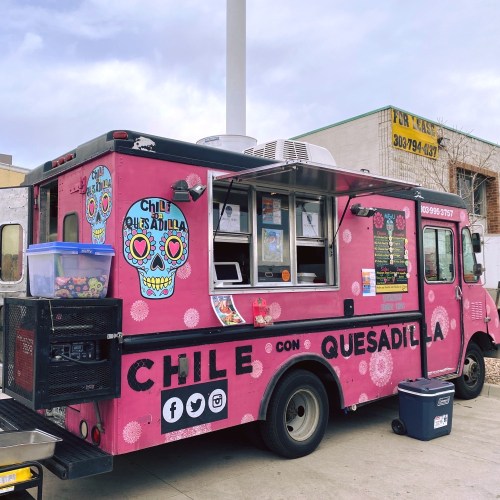 A colorful food truck with a pink exterior, featuring a menu and decorative sugar skull designs.
