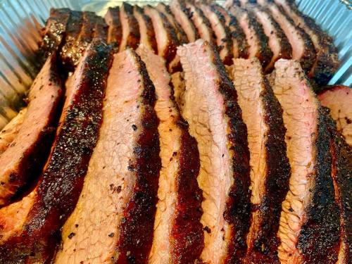 Sliced smoked brisket arranged in a tray, showcasing a smoky crust and tender pink meat.