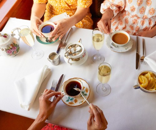 A table set for tea with three people holding cups, sparkling drinks, and a teapot, surrounded by elegant tableware.