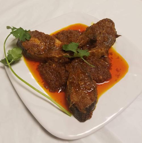 A plate of fish curry garnished with cilantro, served in a rich, spicy sauce.