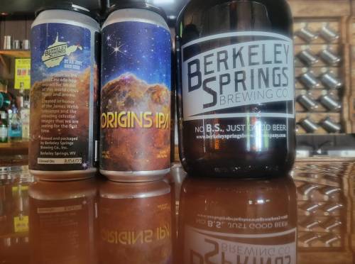 Two cans of Origins IPA and a growler from Berkeley Springs Brewing Co. on a wooden table.