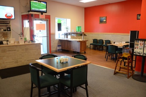 A cozy restaurant interior with a table, chairs, and a TV, featuring a red wall and a buffet area in the background.