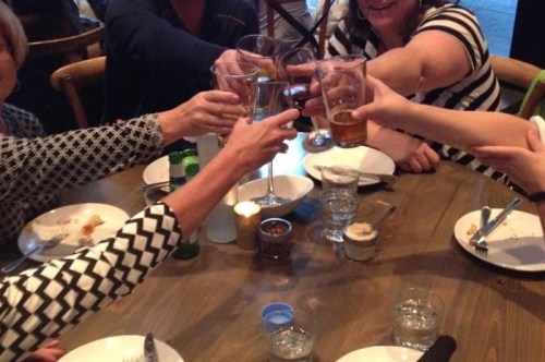 A group of people toasting with drinks at a dining table, surrounded by empty plates and glasses.