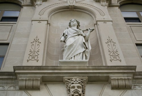 A detailed stone statue of a woman holding a bowl, set against an ornate building facade.