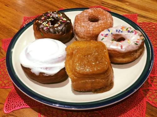 A plate of assorted donuts: chocolate frosted, glazed, and sprinkled varieties, with a cinnamon roll in the center.