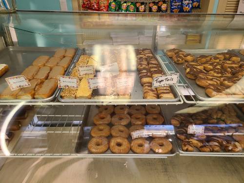 A display case filled with various baked goods, including donuts, pastries, and cookies, with labels for each item.