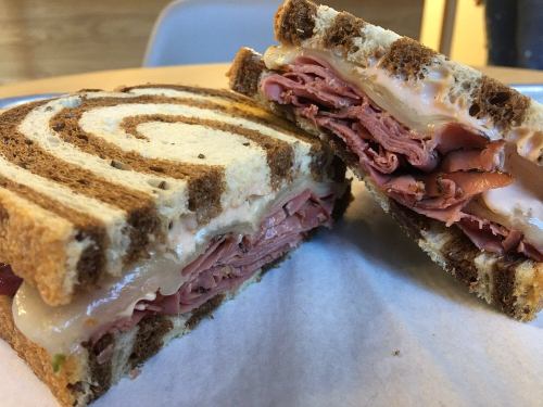 A close-up of a sliced sandwich with layers of deli meat and cheese, served on swirled rye bread.