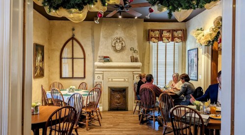 Cozy restaurant interior with wooden tables, chairs, and festive decorations, featuring a fireplace and soft lighting.