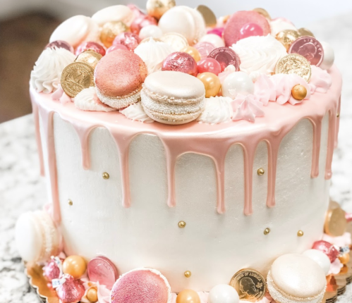 A beautifully decorated cake with pink drip icing, macarons, and colorful candies on top.