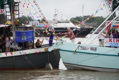 Two boats decorated with colorful flags and banners, docked in a harbor with people celebrating.