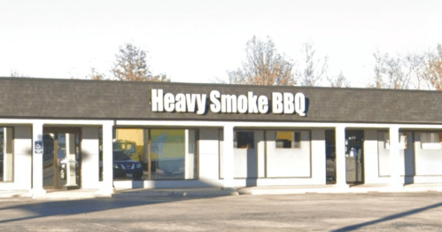 Exterior of a restaurant building with a sign that reads "Heavy Smoke BBQ." Clear sky and trees in the background.