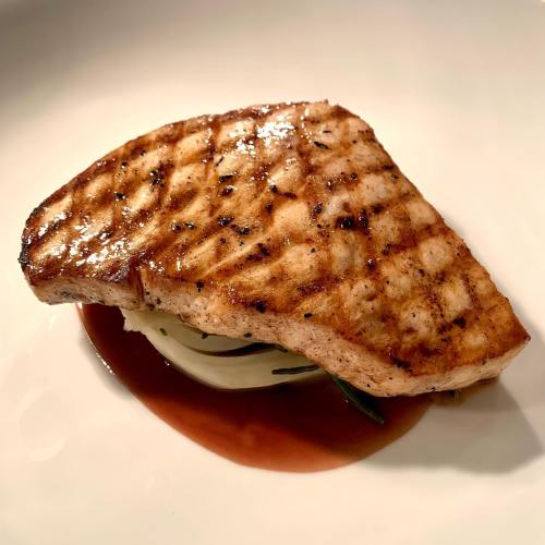 Grilled fish fillet with a seared surface, served on a bed of vegetables and drizzled with sauce.