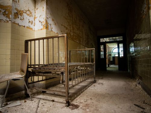 Abandoned hospital room with a rusty bed, a chair, and peeling walls, creating a haunting atmosphere.