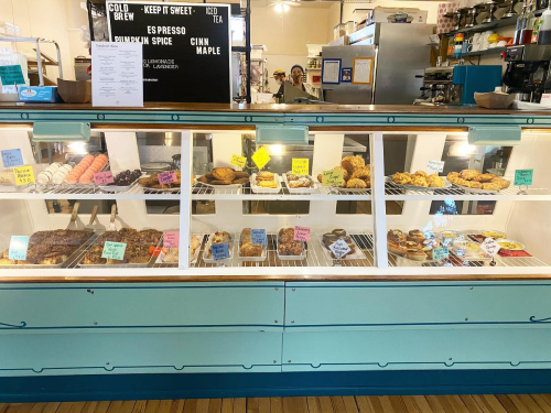 A display case filled with various baked goods, including donuts, pastries, and macarons, in a cozy café setting.