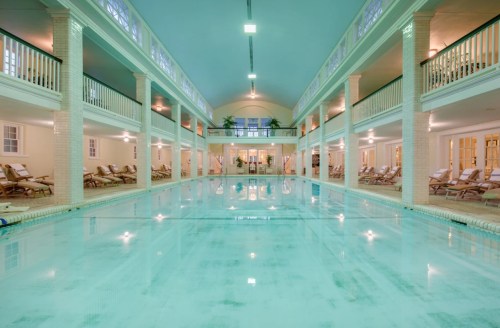 Indoor swimming pool with lounge chairs, tall columns, and large windows, creating a serene and spacious atmosphere.