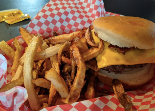 A cheeseburger with melted cheese on a bun, served with a side of golden, crispy French fries in a red checkered basket.