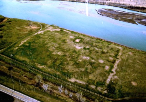 Aerial view of a grassy area near a river, with patches of bare ground and a road along the edge.