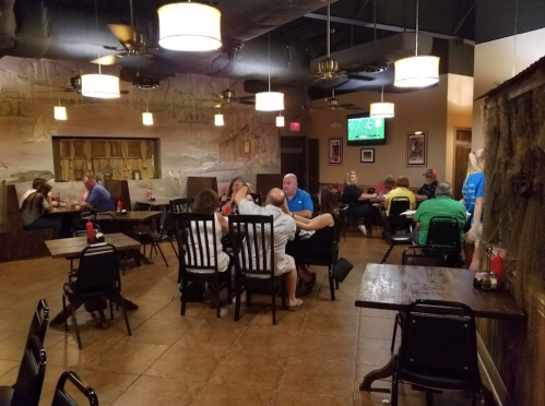 A casual restaurant interior with diners at tables, featuring a rustic decor and a TV in the background.