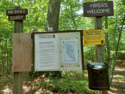 Signpost in a wooded area with notices for hikers, including a map and rules from the Audubon Society of Rhode Island.