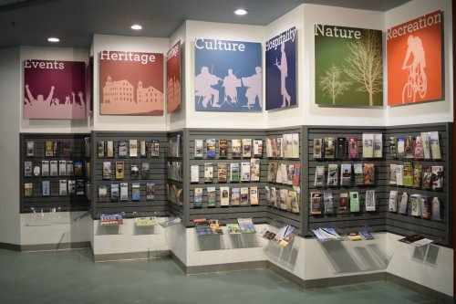A display wall featuring brochures on events, heritage, culture, nature, and recreation in a public space.