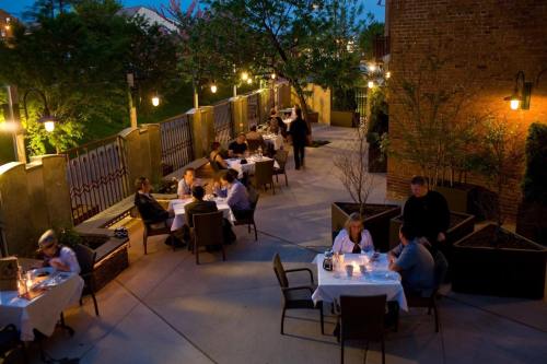 Outdoor dining scene at dusk, with tables set for guests and warm lighting creating a cozy atmosphere.