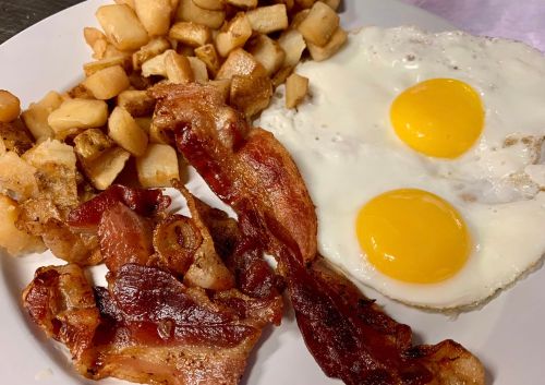 A plate of breakfast featuring two fried eggs, crispy bacon, and golden-brown diced potatoes.
