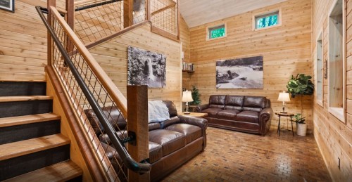 Cozy wooden interior with a staircase, leather sofas, and large windows, creating a warm, inviting atmosphere.