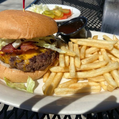 A juicy cheeseburger with bacon, lettuce, and pickles, served with a side of golden fries and dipping sauce.