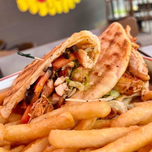 A close-up of a grilled chicken wrap filled with vegetables, served with a side of golden French fries.