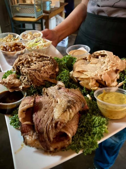 A platter of assorted meats on a bed of greens, accompanied by small containers of sauces and side dishes.