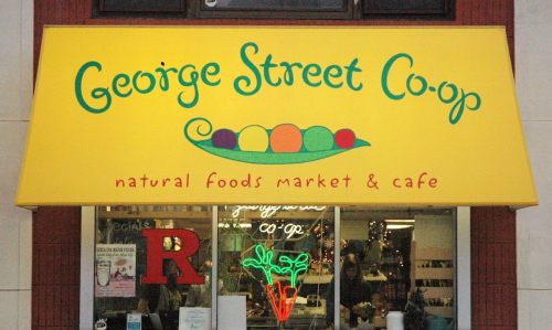 Bright yellow storefront sign for George Street Co-op, featuring colorful peas and text about natural foods market and café.