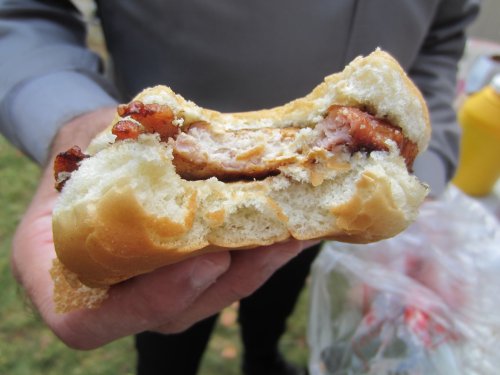 A close-up of a partially eaten sandwich with meat and bacon, held in a person's hand.