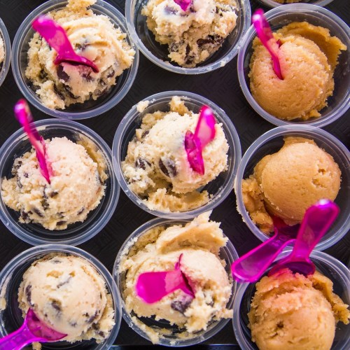 Colorful ice cream scoops in clear cups, featuring chocolate chip and orange flavors, each with a pink spoon.