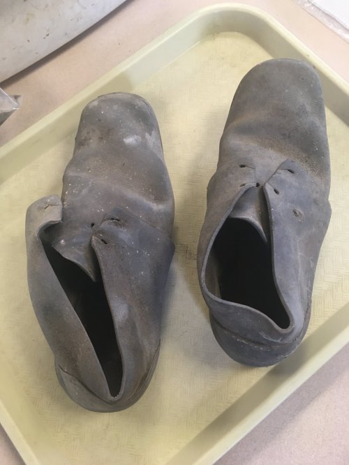 Worn, dusty black rubber shoes displayed on a light-colored tray.