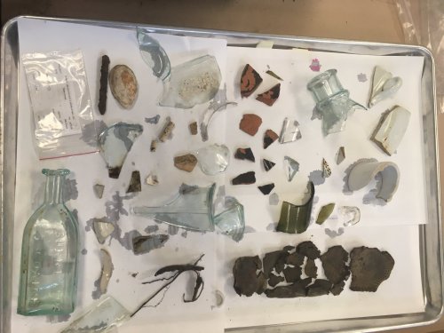 A tray displaying various pieces of glass and ceramic artifacts, including broken bottles and pottery shards.