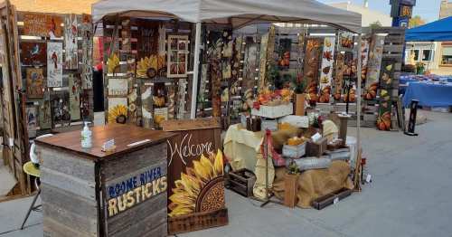 A rustic market booth displaying wooden crafts, signs, and autumn decorations, with a welcoming atmosphere.
