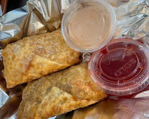 Two crispy fried egg rolls on foil, accompanied by sweet and sour sauce and a red dipping sauce in plastic containers.