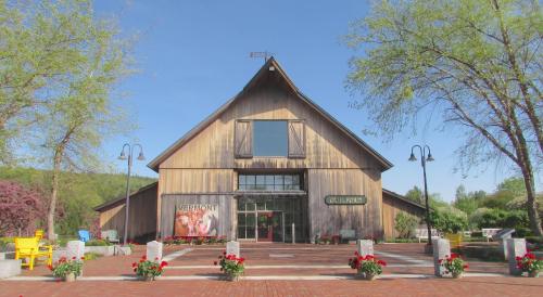 A large wooden barn with a glass entrance, surrounded by flowers and trees, set in a scenic outdoor area.