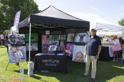 A man stands beside a photography booth featuring various portraits at an outdoor event.