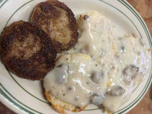 A plate of biscuits topped with creamy sausage gravy, accompanied by two crispy sausage patties.