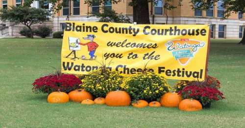 A colorful banner at Blaine County Courthouse welcomes visitors to the Watonga Cheese Festival, surrounded by flowers and pumpkins.