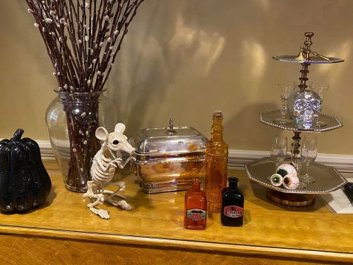 A decorative display featuring a skeleton rat, vintage bottles, a silver container, and a skull-shaped glass.