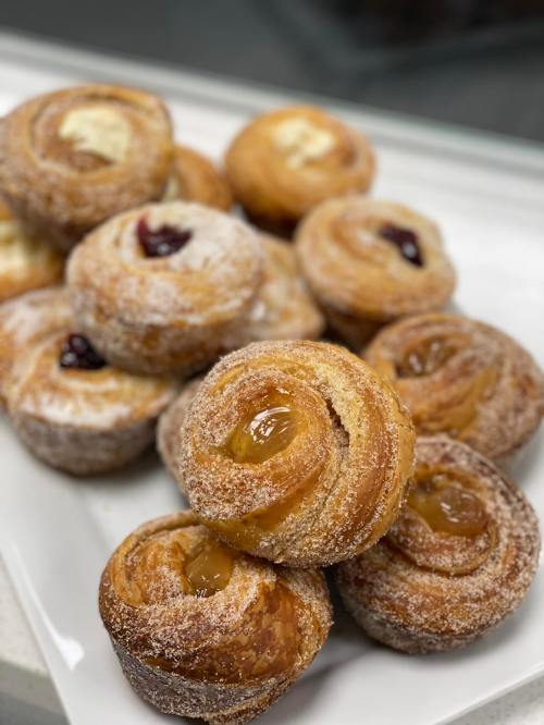 A plate of freshly baked pastries, featuring sweet rolls with various fruit fillings and a dusting of sugar.